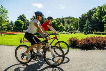 Dwie osoby na rowerach cieszą się piękną pogodą w parku. To pokazuje, co daje jazda na rowerze: aktywność, relaks i kontakt z naturą.