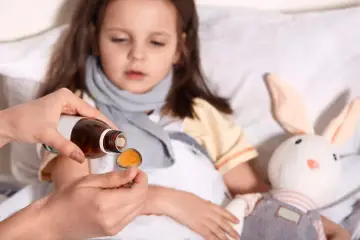 Dziecko w łóżku, mama podaje lek na łyżeczce. Ważne jest, jak dawkowac leki przeciwgorączkowe dziecku, by szybko poczuło ulgę.