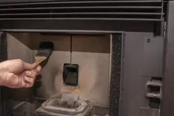 Main d'une personne nettoyant la chambre de combustion d'un poêle à pellet MCZ avec une brosse. Un problème de nettoyage peut causer des dysfonctionnements.