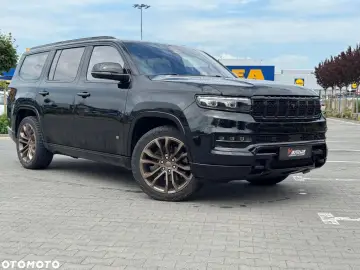 Czarny Grand Wagoneer z brązowymi felgami stoi na parkingu przed sklepami.