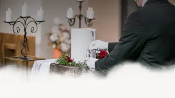 Uroczystość pogrzebowa w Toruniu. Biała urna, zdjęcie zmarłej, róże i świece.
