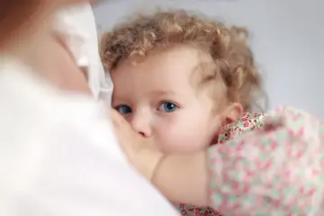Bambina con occhi azzurri e capelli ricci, stretta al petto della madre. Un'immagine che evoca il legame profondo, ma anche le possibili conseguenze psicologiche dell'allattamento prolungato.