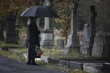 Smutna kobieta z parasolką i czerwonymi różami na cmentarzu. Pamiętaj, dlaczego nie wolno przynosić rzeczy z cmentarza do domu.