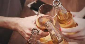 Ludzie wznoszą toast butelkami piwa i kieliszkiem z bursztynowym płynem. Pytanie: czy po szczepieniu można pić alkohol?
