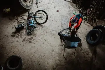 Przygotowania do rajdu rowerowego. Dwóch mężczyzn naprawia rower w garażu, otoczeni oponami i narzędziami.