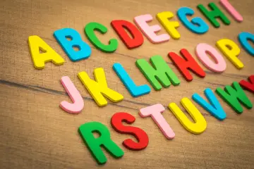 Kolorowe litery alfabetu, od A do W, ułożone na drewnianym tle. Idealne do nauki, jak w szkole francuskie r.