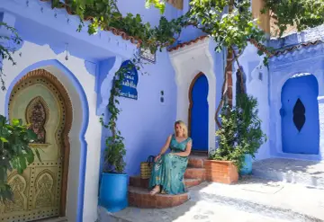 Maj w Maroku to idealna pogoda na zwiedzanie błękitnego miasta Chefchaouen. Kobieta w letniej sukience siedzi na schodach przed Casa Sabila.