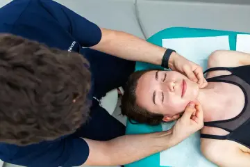 Fizjoterapeuta wykonuje zabieg fizjoterapii stomatologicznej, delikatnie masując twarz pacjentki.
