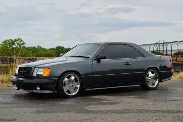 Ciemnoszary Mercedes "Hammer" coupe z przyciemnianymi szybami i chromowanymi felgami stoi na mokrej drodze.