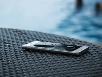 Smartfon z kroplami wody na ekranie, leżący na plecionej powierzchni. Dowód, że IP68 co oznacza: odporność na zanurzenie.