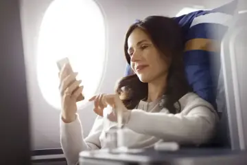 Kobieta w samolocie korzysta z telefonu, sprawdzając, czy w samolocie jest wifi.