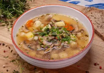 Jak zrobić zupę pieczarkową? Aromatyczna zupa z pieczarkami, ziemniakami i marchewką, udekorowana szczypiorkiem i tymiankiem, podana z chlebem.