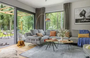 Nowoczesny salon z szarą sofą, stolikami kawowymi i widokiem na las. Inspiracja, jak urządzić salon, by był przytulny i stylowy.