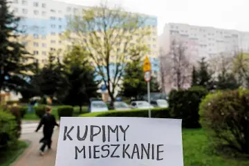 Znak "Kupimy mieszkanie" na tle bloków mieszkalnych. Co zrobić, gdy nie stać nas na mieszkanie? Szukamy rozwiązań.