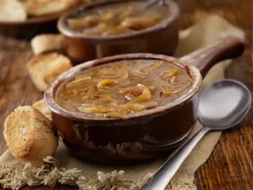 Zupa cebulowa w brązowej miseczce z grzankami i łyżką na drewnianym stole.