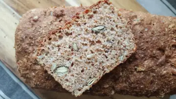 Kromka chleba żytniego z pestkami na drewnianej desce.