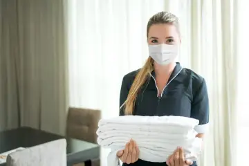 Pracownica hotelu w maseczce niesie stos czystych ręczników. Odpowiedź na pytanie: czy w hotelach są ręczniki - tak!