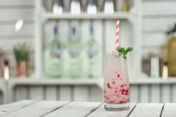 Orzeźwiający drink z granatem i miętą, idealny na toast "cin cin". Na półce w tle widać butelki alkoholu.