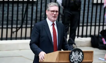 Keir Starmer, premier Wielkiej Brytanii, przemawia przy mównicy z herbem królewskim.