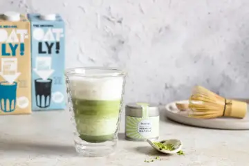 Warstwowy napój matcha z pianką, obok puszka z matchą i bambusowa miotełka. Idealny przepis, jak zrobic matche.