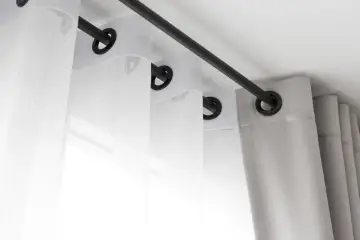 Białe i szare zasłony z metalową przelotką wiszą na czarnym karniszu.