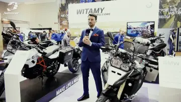Mężczyzna w garniturze prezentuje motocykl BMW 800 na targach. Obok stoją inne maszyny BMW.