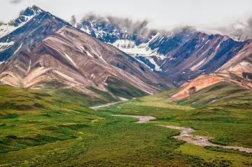 Malowniczy krajobraz w parku narodowym w USA, Alaska. Kręta rzeka płynie przez zieloną dolinę u stóp skalistych, ośnieżonych gór.