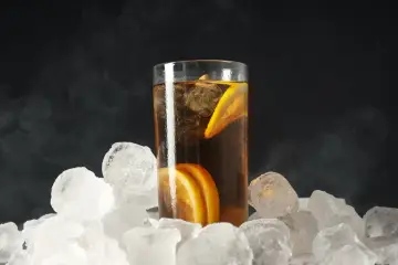 Szklanka long drink z lodem i cytryną, otoczona bryłami lodu, tworzy chłodny klimat. Zbyt duża ilość lodu może szybko rozcieńczyć napój.