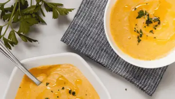 Deux bols de velouté de butternut facile, ornés d'huile d'olive et de persil frais, prêts à être dégustés.