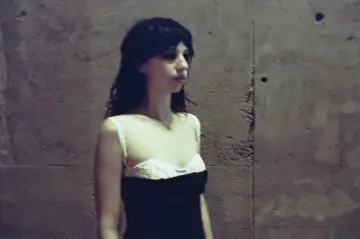 Stella Rose Gahan w czarnej sukience z białym gorsetem, stoi przy betonowej ścianie.