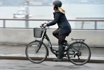 Kvinna cyklar på en elcykel, kanske med bidrag för att underlätta pendlingen. Hon bär hjälm och en varm jacka.