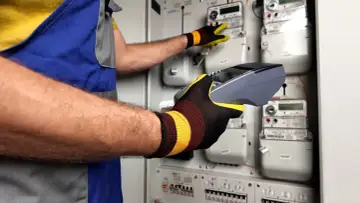 Technik w rękawicach obsługuje licznik energii elektrycznej, przygotowując dokumentację do Tauron reklamacje.