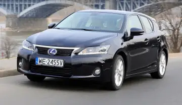 Czarny Lexus CT 200h jedzie po drodze, z mostem w tle.