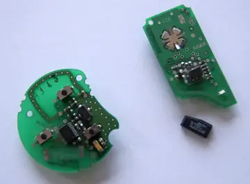 Dwa zielone układy elektroniczne, jeden okrągły, drugi podłużny, z widocznymi elementami i chipem. Obok leży mały czarny chip, prawdopodobnie kluczowy element immobilizera.