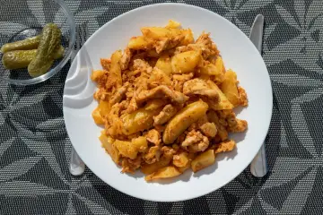 Pyszne danie z kurczakiem i ziemniakami, przypominające smaki kuchni węgierskiej. Obok miseczka ogórków kiszonych.