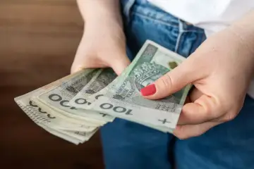 Dłonie trzymające stos banknotów 100 zł. Czy to już kwota bazowa służba cywilna 2026?