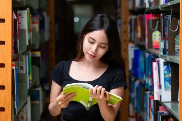 Młoda kobieta w bibliotece, pochłonięta lekturą, zastanawia się, od jakiej średniej stypendium w podstawówce mogłaby otrzymać.