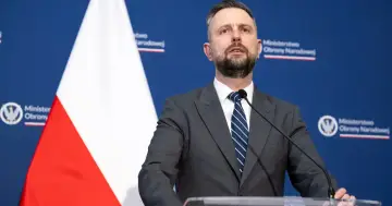 Minister obrony narodowej przemawia na tle flagi Polski i logo ministerstwa.