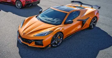 Pomarańczowy Chevrolet Corvette C8 z czarnym dachem i spojlerem na torze wyścigowym. Obok widać fragment czerwonego samochodu.