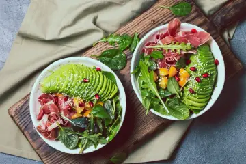 Dwie miski z sałatką z awokado, szynką parmeńską i granatem. Idealna keto kolacja, pełna zdrowych tłuszczów i witamin.