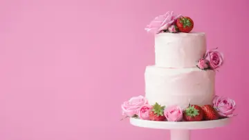 En vacker tvåvåningstårta med rosa frosting, dekorerad med rosor och jordgubbar. Perfekt för ett sommarbröllop eller en fest. Ett enkelt tårta recept att följa.
