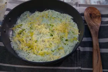 Kasza manna na słono, przygotowana na patelni, posypana startym serem i ziołami. Obok drewniana łyżka.