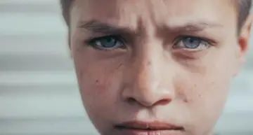 Zamyślony chłopiec z niebieskimi oczami, zmartwiony wyraz twarzy. To mogą być objawy parentyfikacji, gdy dziecko przejmuje role dorosłych.