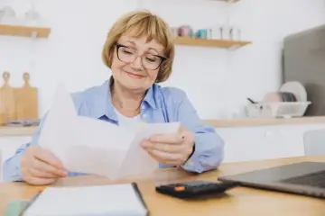 Uśmiechnięta starsza pani z okularami przegląda dokumenty, planując wymianę dowodu osobistego po 70 roku życia.
