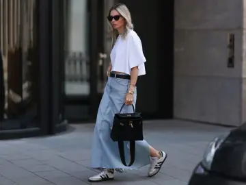 Kobieta w białej bluzce i długiej spódnicy jeansowej, z czarną torebką i sneakersami. Stylowe długa spódnica jeansowa stylizacje.