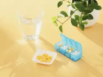 Un bicchiere d'acqua, una ciotolina con capsule gialle e un portapillole blu. Forse integratori per capire cosa sono gli elettroliti.