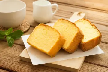 Szybkie ciasto z 4 składników, pokrojone na kromki, leży na desce. Obok filiżanka i dzbanuszek.