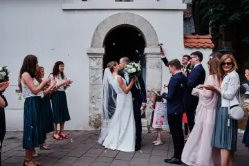 Para młoda całuje się przed kościołem, goście sypią bańki mydlane. To piękny ślub jednostronny, pełen radości i miłości.