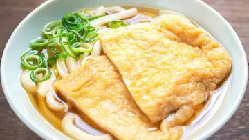 Pyszna zupa z makaronem udon z dwoma kawałkami smażonego tofu i zieloną cebulką.