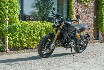 Czarny Ducati Scrambler 1100, gotowy na przygodę, zaparkowany przy ceglanej ścianie porośniętej bluszczem.